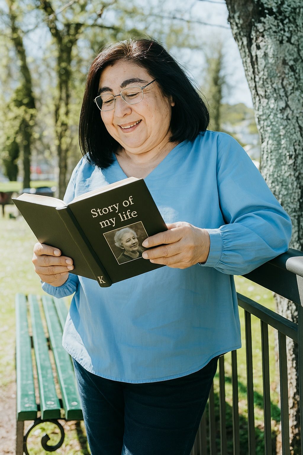 Woman joyfully reading Story of My Life keepsake book in park